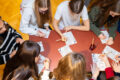 Jugendliche sitzen an einem Tisch und füllen gemeinsam Quiz-Zettel aus.