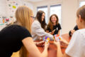 Jugendliche spielen lachend das COCO-Kartenspiel am Tisch.