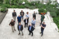 Das Foto zeigt eine Gruppe von elf Personen – das G&WM Team – die in einem Hof mit Steinplatten und Grünflächen steht. Die Gruppe blickt nach oben zur Kamera, die von oben fotografiert.